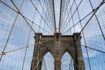 Naklejka premium Słynny most Brooklyn Bridge w Nowym Jorku w Stanach Zjednoczonych Ameryki, przedstawiający zawieszenie przewodowe i flagę USA na szczycie kolumny w częściowo pochmurny dzień z niebieskim Skys.