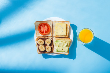 Sandwiches on a white plate, a glass with orange juice, a blue background. Concept of healthy eating, breakfast at the hotel, diet. Natural lighting, hard light. Flat lay, top view.