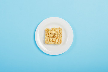 Asian instant noodles on a white plate against a blue background. The concept of convenience foods, fast food, junk food. Flat lay, top view.
