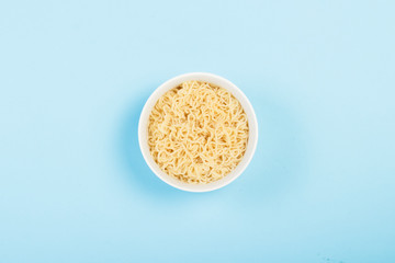 Asian instant noodles on a white plate against a blue background. The concept of convenience foods, fast food, junk food. Flat lay, top view.