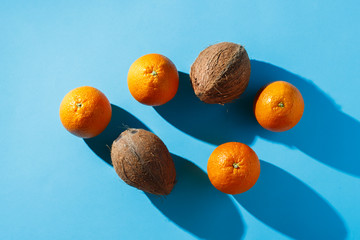 Oranges and coconuts on a blue background. Hard light. Tropics concept, healthy food, breakfast, diet, vacation. Flat lay, top view.