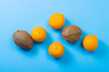 Coconuts and oranges on a blue background. Concept of tropical fruits, vacation and travel, diet and weight loss. Flat lay, top view.
