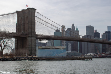 Obraz premium The famous Brooklyn Bridge Bridge located in New York City in the United States of America showing the suspension wired and the USA flag at the top of the column on a part cloudy day with blue Skys.
