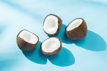 Fototapeta na wymiar Broken coconut on a blue background under natural light with shadows. Hard light. Concept of diet, healthy eating, rest in the tropics, vacation and travel, vitamins.