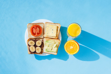 Sandwiches on a white plate, a glass with orange juice, a blue background. Concept of healthy eating, breakfast at the hotel, diet. Natural lighting, hard light. Flat lay, top view.