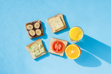 Sandwiches, glass with orange juice, oranges, blue background. The concept of healthy eating, breakfast at the hotel, diet. Natural lighting, hard light. Flat lay, top view.