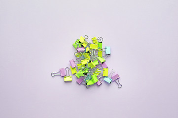 Top view of many multicolor binders clips on pastel purple background.Trendy neon colors. Group of paper clip different colors.