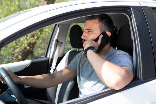 Man talking at mobile phone while driving a car. - Powered by Adobe