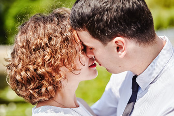 Kissing couple in love. Portrait of a young curly hair woman and brunette man. Bride and groom outdoor. Manifestation of tender feelings