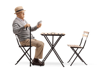 Senior man with a cane sitting at a table and playing cards