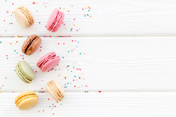 Brignt macarons for sweet break on white wooden background top view mock up