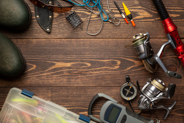 Fishing theme. Frame with rubber boots, fishing box, reels, fishing buoy, rod, compass, feeder, knife and fish string on wooden background. Free space