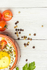 Portioned baked eggs in ceramic cocotte on white wooden table, breakfast. Top view, copy space for you text.