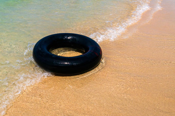 Black rubber loop with soft wave of blue ocean in outdoor sun lighting on sandy beach. Background of travel in summer season © leaw197340
