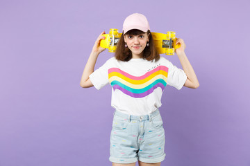 Portrait of smiling beautiful teen girl in vivid clothes holding yellow skateboard isolated on violet pastel wall background in studio. People sincere emotions, lifestyle concept. Mock up copy space.