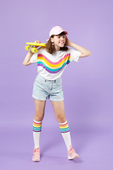 Smiling teen girl in vivid clothes holding yellow skateboard, looking aside, putting hand on head isolated on violet pastel background. People sincere emotions, lifestyle concept. Mock up copy space.