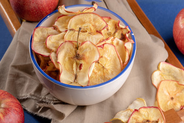 Close-up cup with apple chips ans fresh red apples on beige cloth.