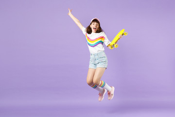 Joyful teen girl in vivid clothes holding yellow skateboard, having fun, jumping, spreading hands isolated on violet pastel background. People sincere emotions, lifestyle concept. Mock up copy space.