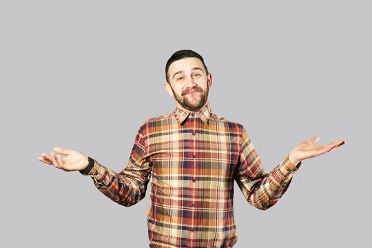 Young handsome man with facial hair posing over gray wall with a lot of copy space for text. Portrait of confident bearded male, wearing hipster slim fit checkered shirt. Isolated, background.