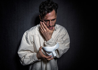 Young attractive man with scars from burns, holding a white theater like mask
