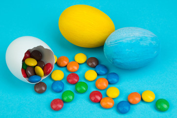 Happy Easter. Broken Easter egg with multi-colored candy decorations on blue background