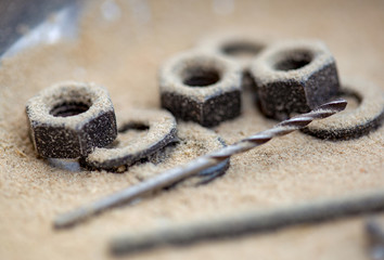 Macro photography of a drill and some nuts and packing rings covered in saw dust, captured at a carpenter workshop in the Andean mountains of central Colombia.
