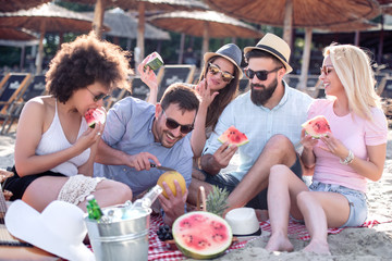 Happy young friends eating watermelon on beach