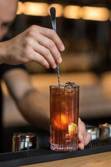 Bartender is adding ingredient in shaker at bar counter.