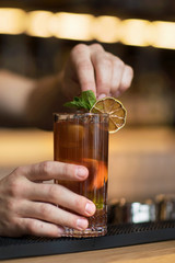 Bartender is adding ingredient in shaker at bar counter.
