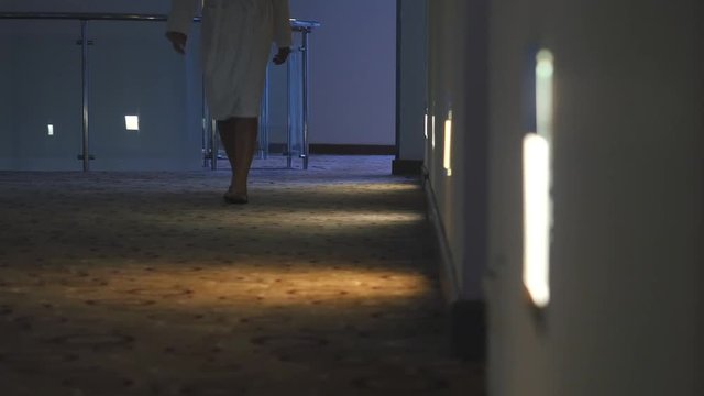 Unrecognized woman  dressed in bathrobe walk in the hotel corridor 