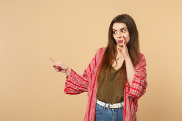 Amazed young woman in casual clothes whispering secret behind her hand, pointing index finger aside...