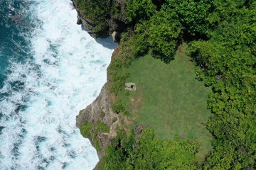 Aerial view of man lying on a green cliff above the blue Indian Ocean and foaming waves, Uluwatu, Bali, Indonesia.