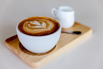 Cup of hot coffee with milk art on the surface placed on wooden table.