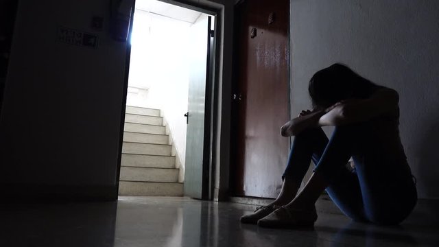 Silhouette of a sad young girl sitting in the dark leaning against the wall in old condo, Domestic violence, family problems, Stress, violence, The concept of depression and suicide.