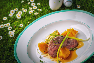 delicious steak with spring vegetables and sauce served on white plate in nature, easter menu for restaurant