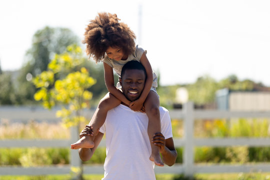 Smiling African American man carrying daughter on shoulders