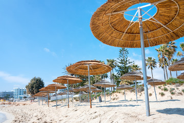 Reed beach umbrellas, sunshades against blue sky on the beach. Bamboo parasols, straw umbrellas on on white sandy tropical seashore. Tropical sea beach coastline, summer holiday.