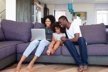 Happy African American family with daughter using laptop at home - Powered by Adobe