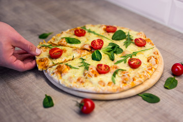 male hand taking slice of tasty pizza with tomatoes and herbs