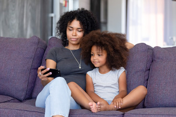 African American woman with daughter using phone together at home