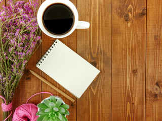 Flat lay,top view grey wooden desk with stationery including notebook and pencil with a cup of coffee,flowers and copy space