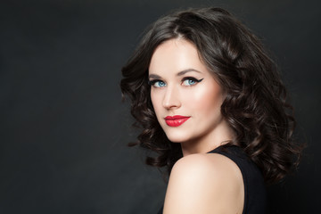 Fototapeta premium Happy woman model with makeup and brown curly hair on blackboard background