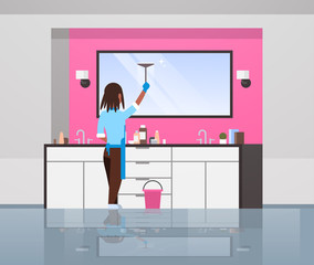 housewife in gloves and apron cleaning mirror with squeegee african american woman doing housework concept modern bathroom interior rear view female character full length