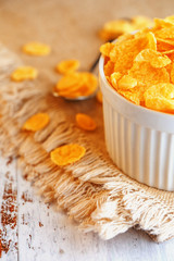 Bowl with golden flakes on a linen, on a light wooden table, next to a spoon. Rustic country style. View from above