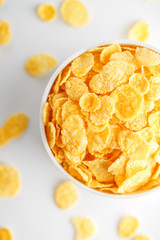 White cup with golden corn flakes, isolated on white background. Hopya crumbled around the cup. View from above. Delicious and healthy breakfast