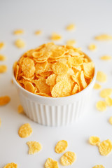 White cup with golden corn flakes, isolated on white background. Hopya crumbled around the cup. View from above. Delicious and healthy breakfast