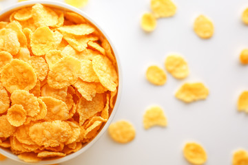 White cup with golden corn flakes, isolated on white background. Hopya crumbled around the cup. View from above