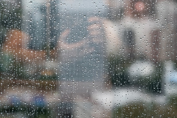 Glass window with raindrops. Overcast day and blurred cityscape outside. Symbol of sadness, depression, sorrow. Abstract texture background with copy space for text and design. Realistic image.