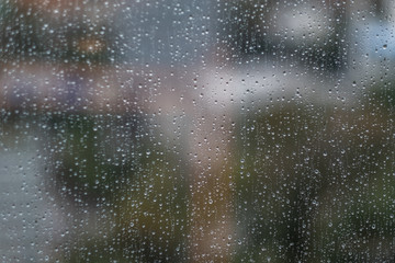 Glass window with raindrops. Overcast day and blurred cityscape outside. Symbol of sadness, depression, sorrow. Abstract texture background with copy space for text and design. Realistic image.