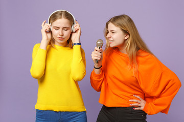 Two young blonde twins sisters girls in colorful clothes listen
